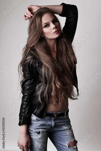 Young girl with long beautiful hair and smoky eyes wearing black leather jacket and jeans . Studio shot.