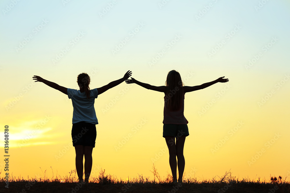 Silhouette of two funny girls on sunset sky background Silhouette of two funny girls on sunset sky background