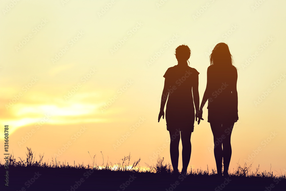 Silhouette of two funny girls on sunset sky background