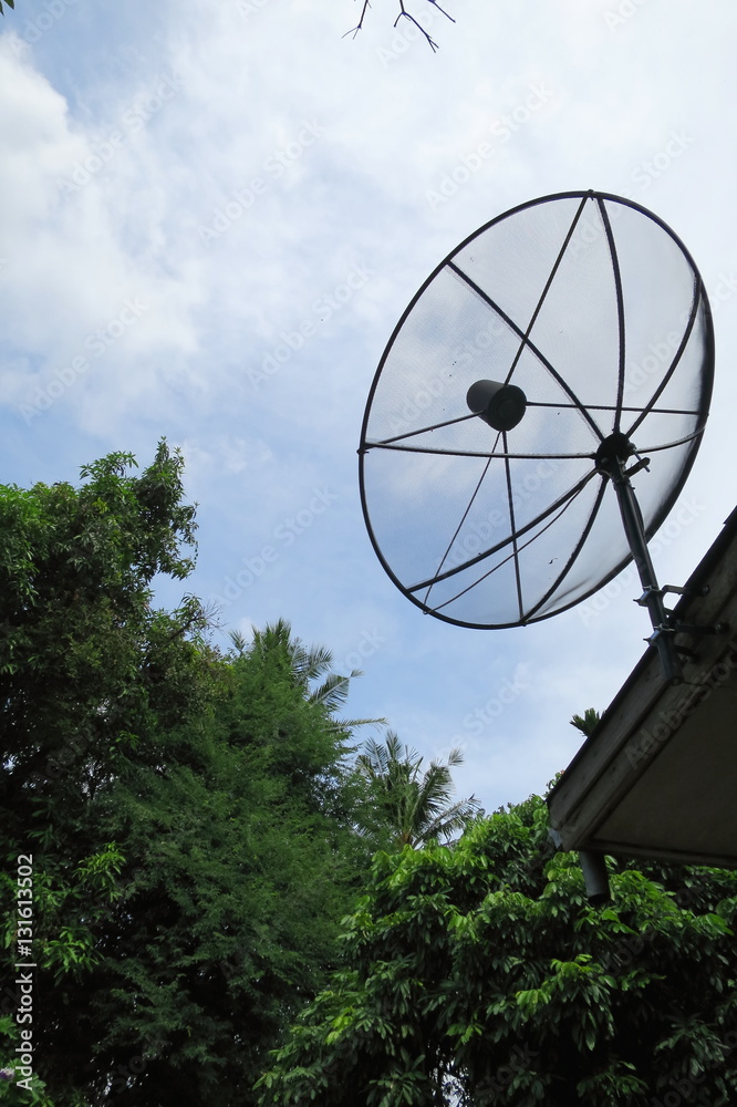 Satellite dish on roof with blue sky and white cloud with tree background.