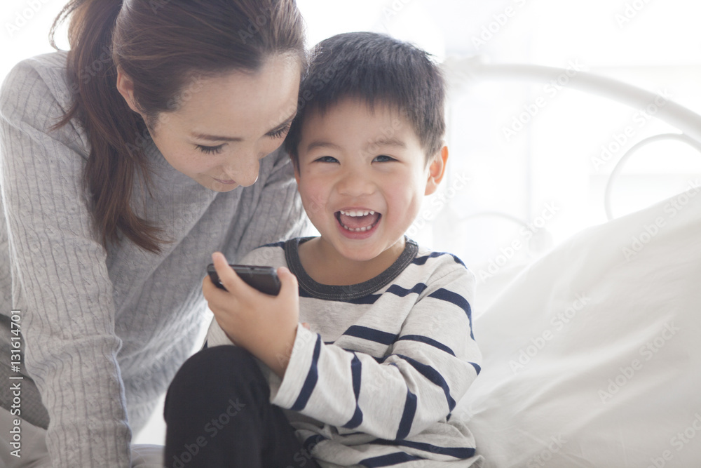 Mother and child are watching smartphone together in the bedroom Mother and child are watching smartphone together in the bedroom