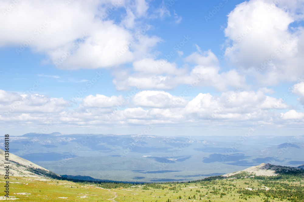 Green mountain valley landscape on a sunny summer day. Clouds shadows on the coniferous forest dark carpet. Path way going through meadow