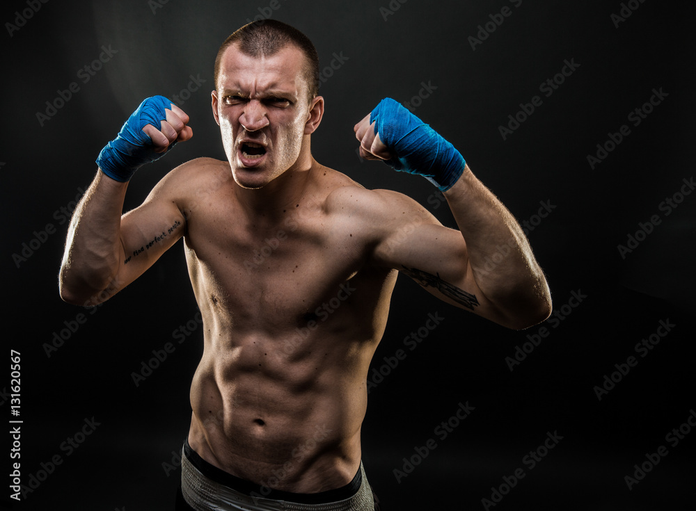 Muscular man standing with mouth opened holding fists up. Studio shot.