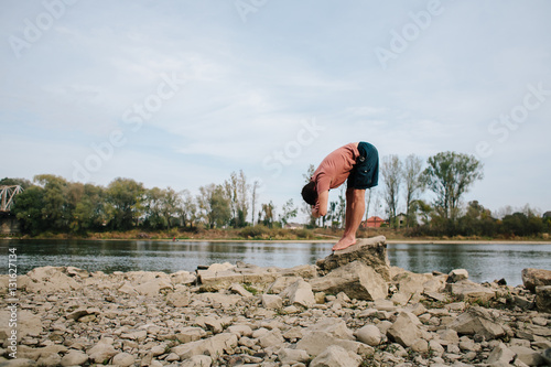 man practices yoga on the river bank