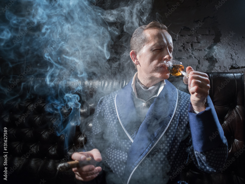 Fototapeta premium Man in his office smoking a cigar and drinking brandy