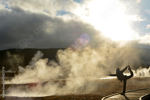 Steam and smoke from the geysers. Silhouette of a girl traveller in yoga pose in Yellowstone national park