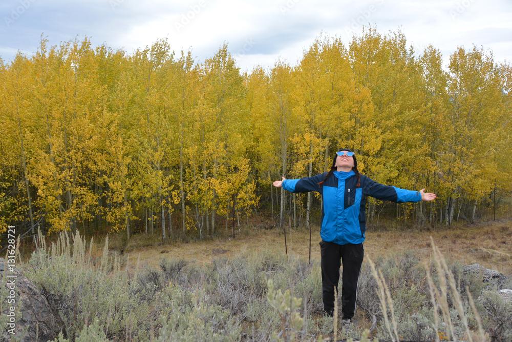 Girl in a blue jacket and blue glasses standing near yellow birches in Yellowstone
