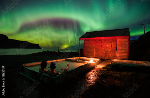Relaxing in geothermal hot pool under northen lights (Aurora Borealis) in Iceland