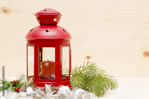 Red metal lantern has a burning candle. Holiday lamp is on the wooden background. 