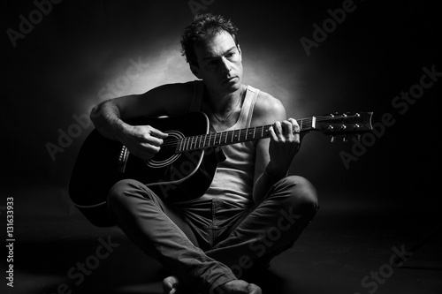 Young caucasian man play a acoustic guitar. Black and white picture, low key studio portrait