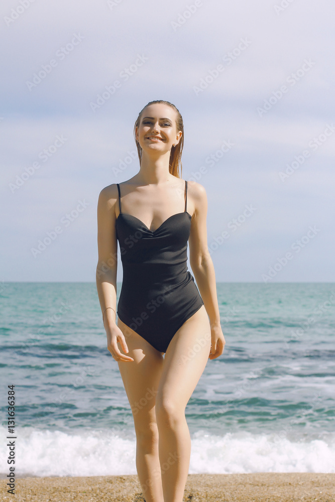 young girl jumping in the sea is engaged in fitness. sexy blonde woman on the beach in a black bathing suit