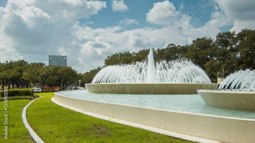 The Mecom Fountain at Hermann Park on a Sunny Day in Houston Tx with Surrounding Traffic and Green Grass Panning Left as Cars Driving Around photo