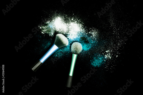 Makeup brushes with powder spilled glitter dust on black background. Light blue powder on black table.