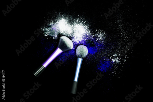 Makeup brushes with powder spilled glitter dust on black background. Blue powder on black table.