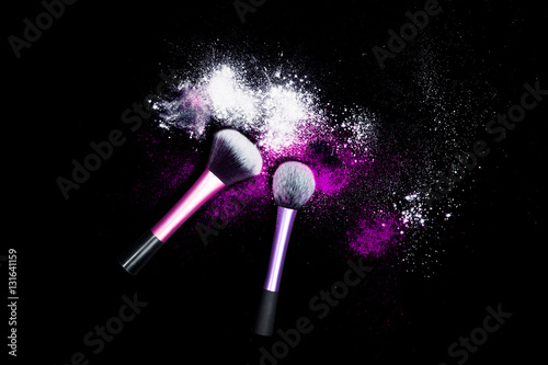 Makeup brushes with powder spilled glitter dust on black background. Purple powder on black table.
