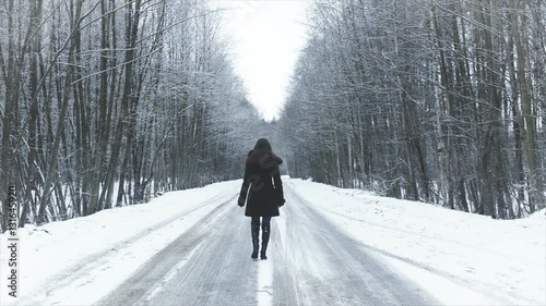 girl walking on the road to the winter woods.
