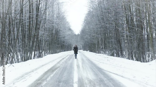girl walking on the road to the winter woods.