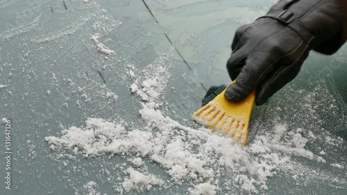 Winter scene, driver hand in glove scraping ice from windshield of car