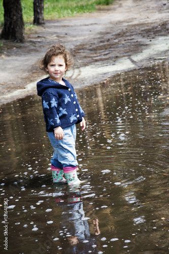 Fototapeta Naklejka Na Ścianę i Meble -  In the spring of funny little girl standing in a pool of rubber