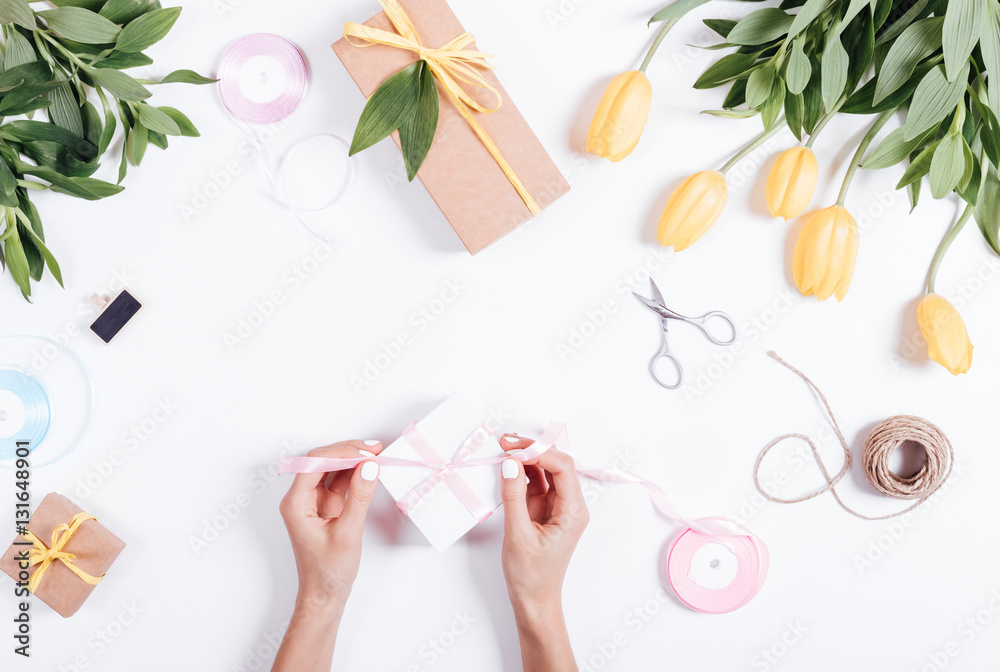 Female hands tie a pink ribbon box with gifts on a white table Female hands tie a pink ribbon box with gifts on a white table