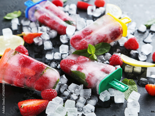 Popsicles with berries on black wooden table