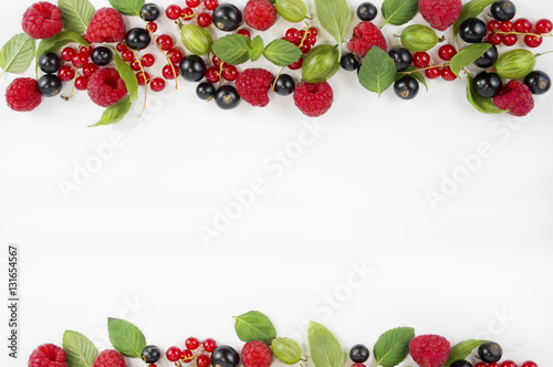 Various fresh summer berries on white background. Ripe raspberries, currants, gooseberries, mint and basil leaves. Berries at border of image with copy space for text.