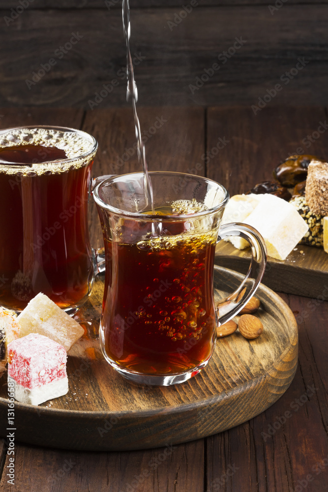 Black tea, oriental sweets, dates and nuts on a dark wooden back