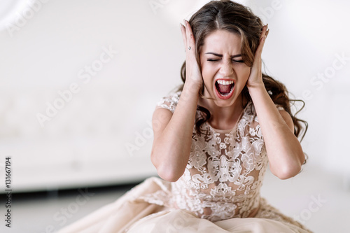 portrait of the bride shouts loudly covering his ears with his hands, furious. Natural light.  photo