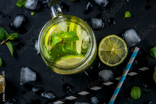 Mojito with lime in a mason jar, with striped straws on a black background with ingredients