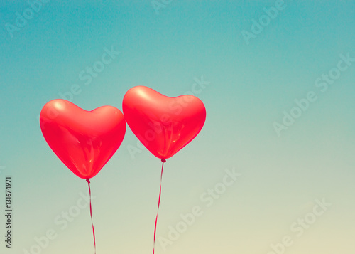 Two red heart shaped balloons in flight