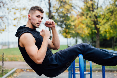 Fototapeta Naklejka Na Ścianę i Meble -  Fitness man doing stomach workouts on horizontal bar outdoors