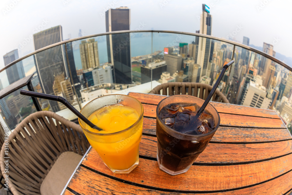 Fototapeta premium cocktail with city skyline view at dusk from skybar. fisheye angle of coke and juice close up.