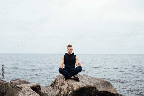 Strong fitness yoga man in lotus pose on the rock beach near the ocean. Harmonic concept.