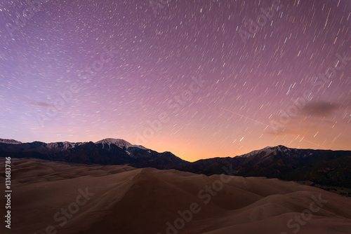 Starry Night at Great Sand Dunes - Star trails of spring night sky over snow peaks and great sand dunes at Great Sand Dunes National Park   Preserve  Colorado  USA.