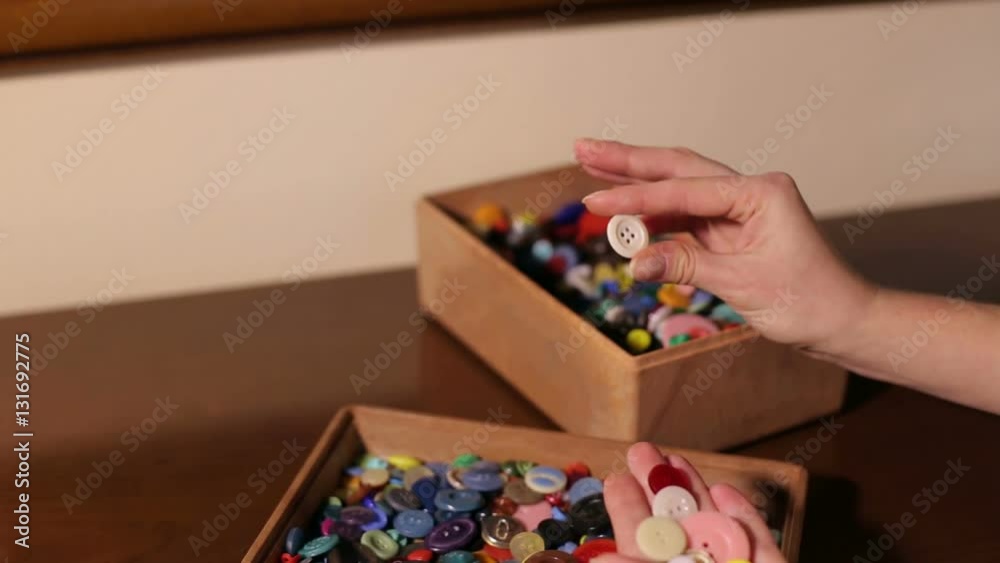 A lot of colorful buttons in a wooden box. The girl looks at the buttons close-up. A lot of colorful buttons in a wooden box. The girl looks at the buttons close-up.