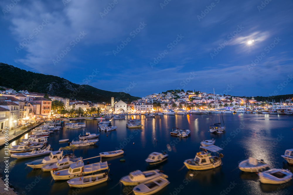 The lights of the old town reflect in the waters of the port of the historic Hvar Town on the island Hvar in Croatia at night with a full moon.