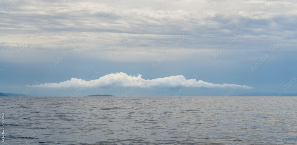 Obraz premium A lone cloud hovers over one of Croatia's Pakleni Islands, a popular tourist destination near Hvar Island.