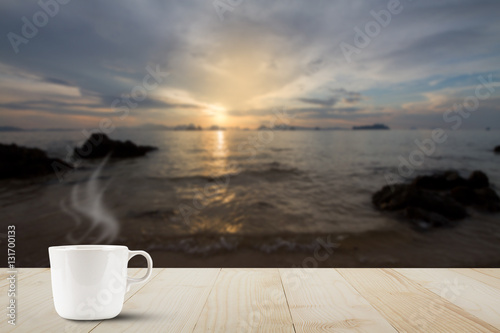 Hot coffee cup with steam on wooden table top on blurred golden sunrise background © shark749