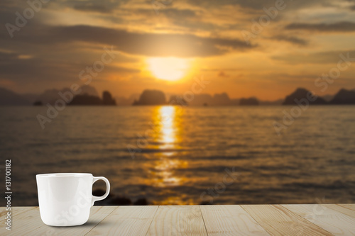 Hot coffee cup on wooden table top on blurred golden sky, sea and island background during sunrise © shark749