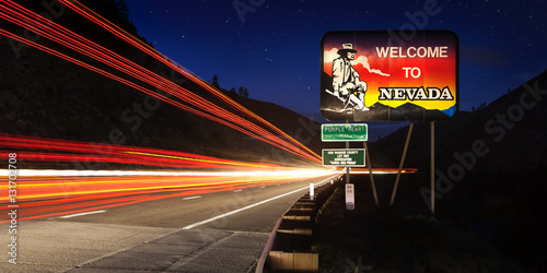 Nevada State line road sign with long exposure traffic trails at night.