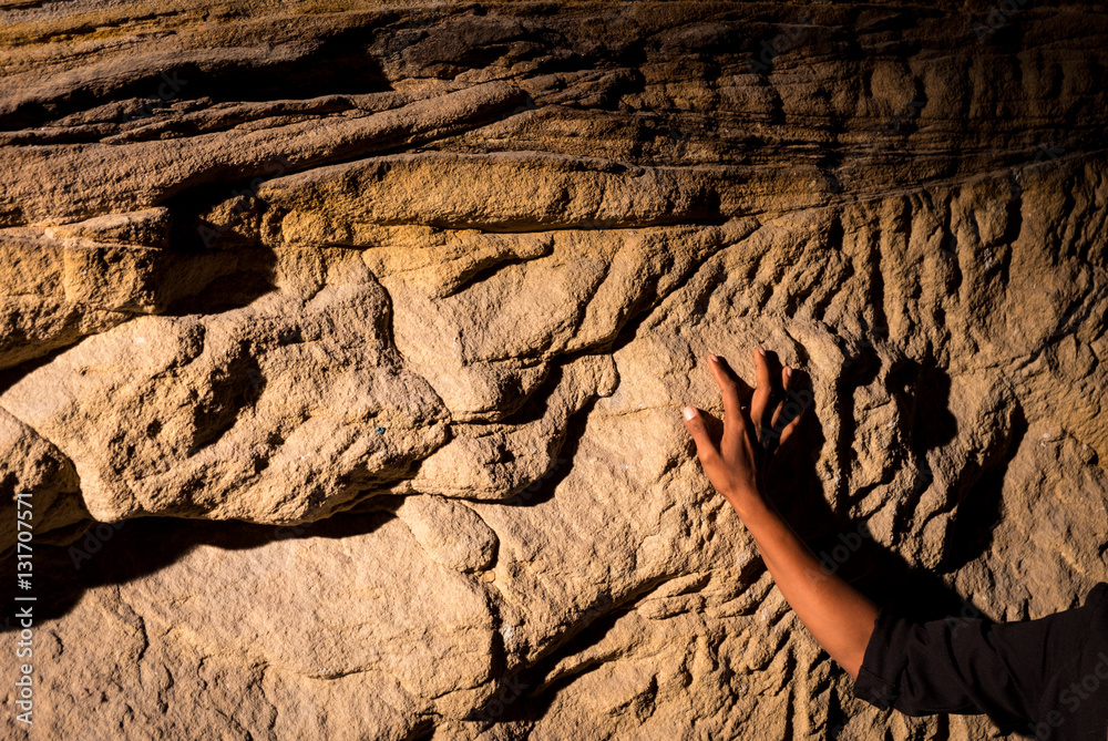 Obraz premium Hand touching rough sandstone rock wall