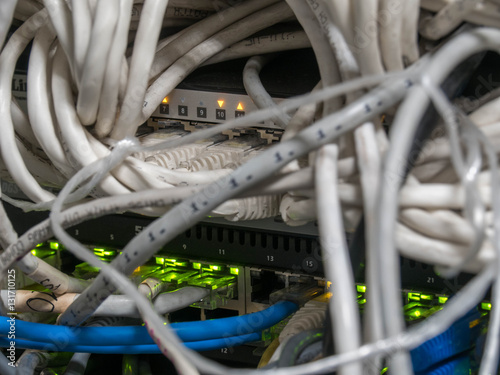 Rows of multiple fiber and ethernet cables plugged into a router (switch), with green activity lights. The network installed in the rack. Data center, wired network, switch panel, rack.