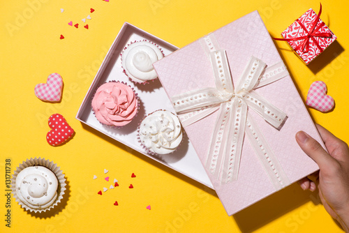 Delicious cupcake with paper box on yellow background