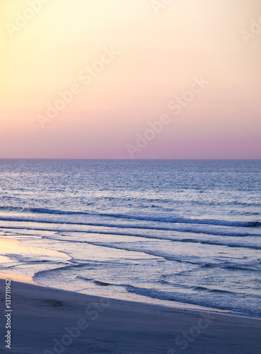 A beautiful scenery of sunset, sky is in orange, purple and violet. The waves hitting the beach.