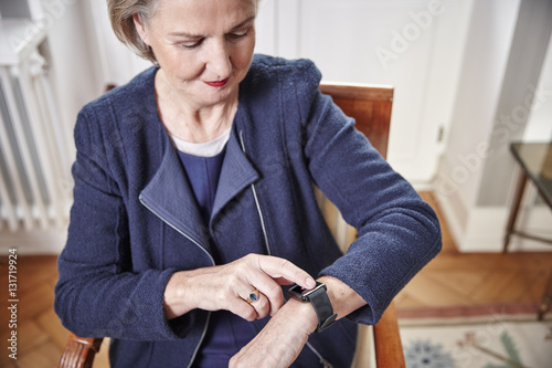 Senior woman sitting on chair looking at smartwatch photo