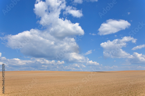 Field of plowed ground on a background of blue sky with clouds.