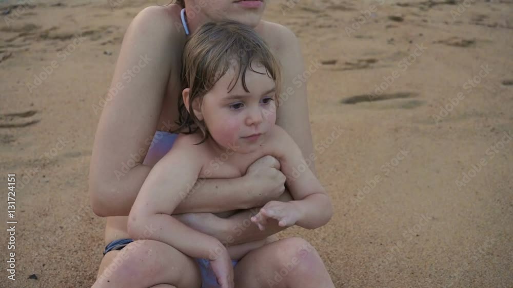 The three-year girl and mother on vacation at sea. Mom keeps daughter in her arms while sitting on the sand. The three-year girl and mother on vacation at sea. Mom keeps daughter in her arms while sitting on the sand.