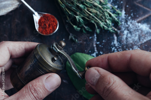 Cooking ingredients - thyme, spices, pepper arranged at the rustic wooden table and a coffee mill in hands