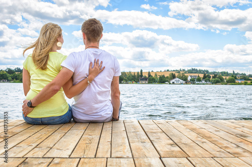 A couple seated on a wooden platform overlooking a river