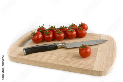 Bunch of cherry tomatoes with green leaves lying on a cutting board, isolated on white background. Still-life studio shot taken with soft-box.